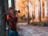 woman leaning back on tree trunk using black dslr camera during day